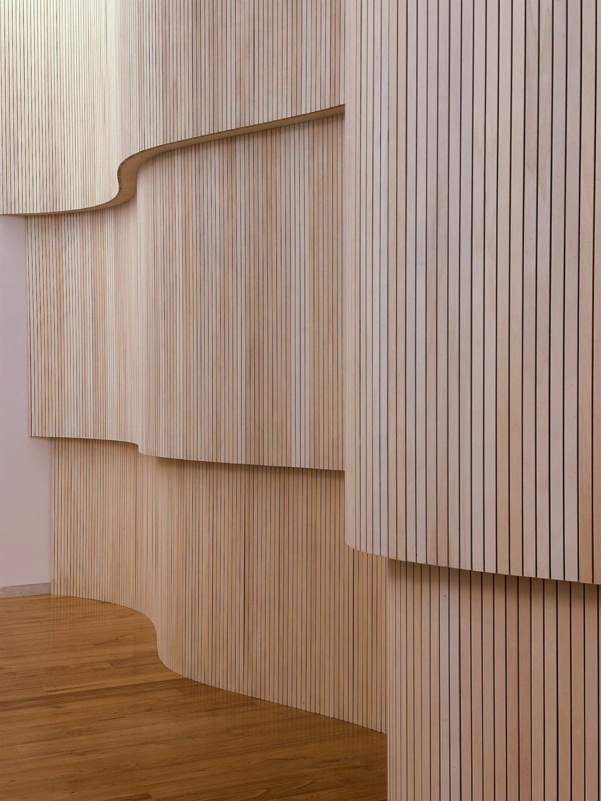 Curved wood-slat wall panelling meeting a wooden floor in an interior