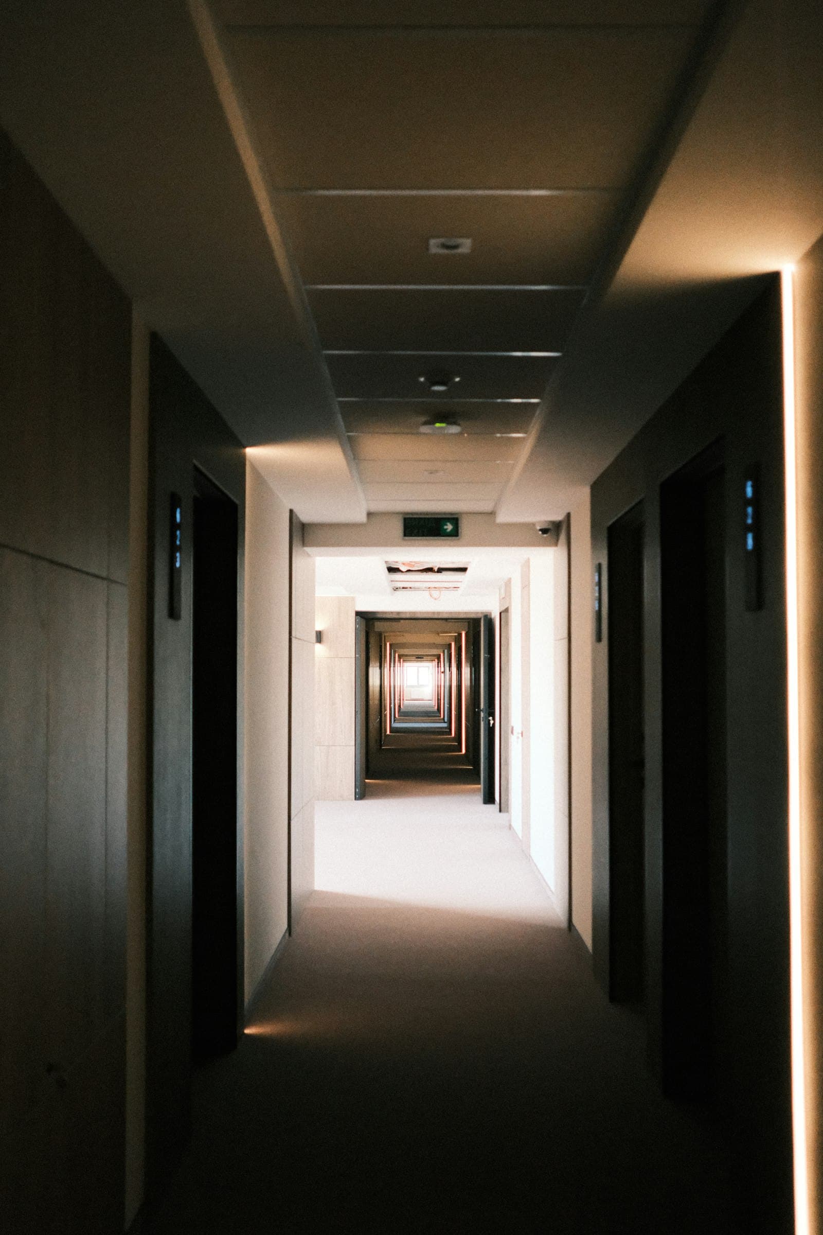A long, dimly lit hotel corridor with receding doorways